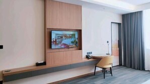 A modern hotel room with a flat-screen TV mounted on the wall, a small table with a chair, and a door with curtains. - Zhengzhong Holiday Hotel (Yixing)