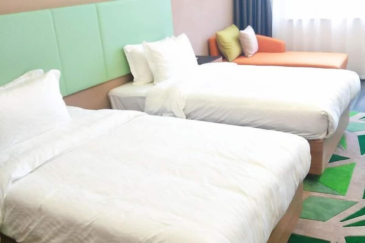 Una habitación de hotel con dos camas, cabecero verde y alfombra estampada.