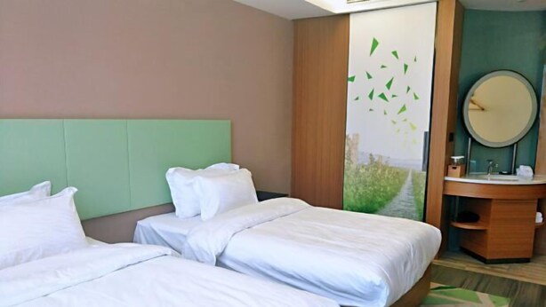 Une chambre d’hôtel avec deux lits, une tête de lit verte, une coiffeuse en bois et un grand miroir.