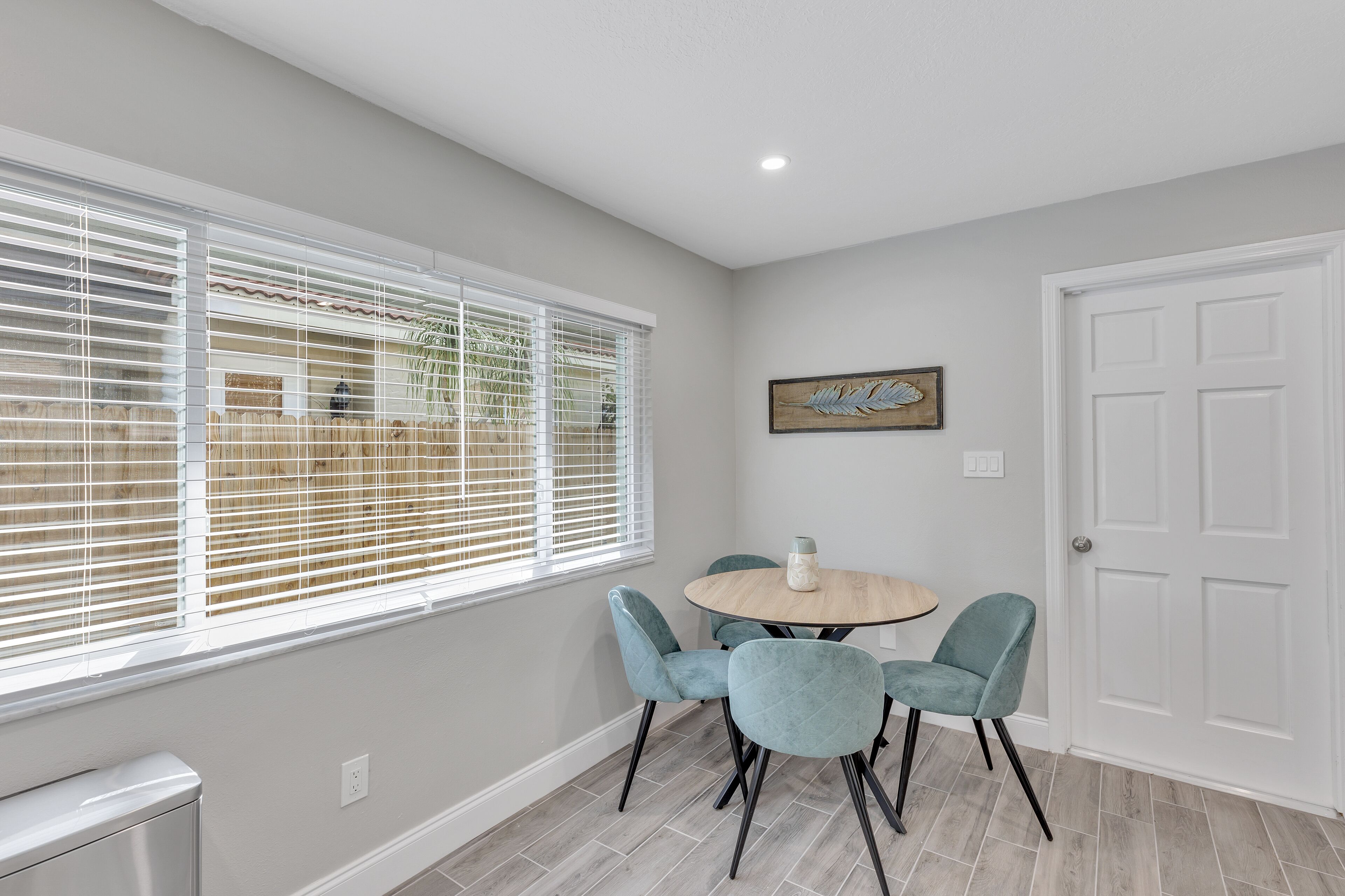 A dining area with a round table, four chairs, and a window with blinds.