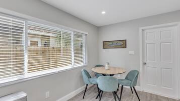 A dining area with a round table, four chairs, and a window with blinds.
