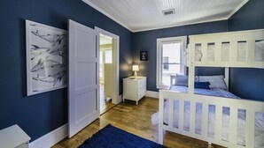 Une chambre avec un lit superposé, une table de chevet avec une lampe, un tableau encadré au mur et une porte donnant sur une autre pièce.