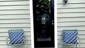 Une terrasse en bois avec deux chaises en osier et une porte noire.