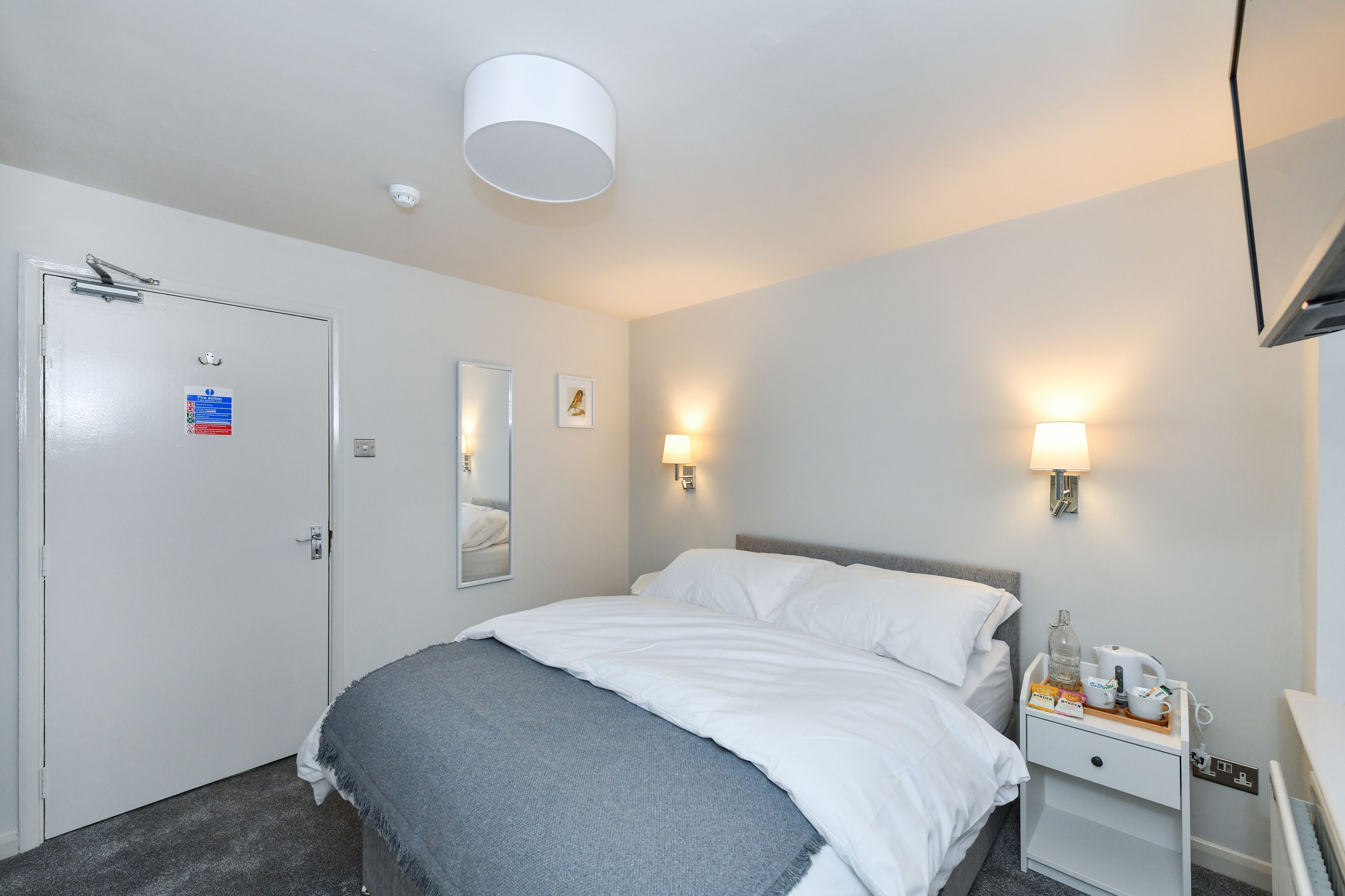 Une chambre d’hôtel avec un lit, une table de chevet, une lampe et une porte avec une pancarte.