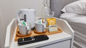 Una bandeja con un control remoto, dos tazas blancas, un vaso, una botella y un paquete de comida.