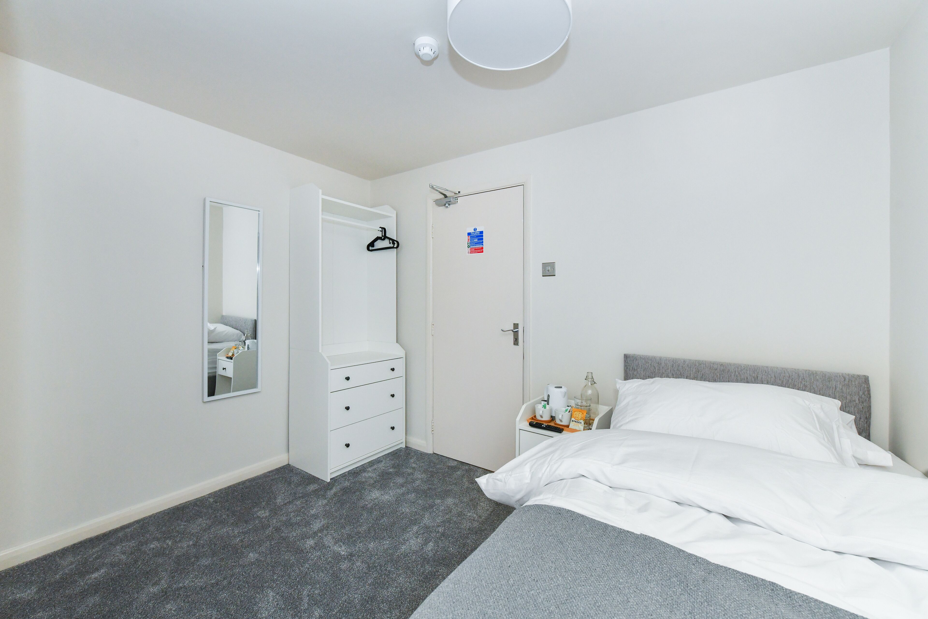 Una camera da letto con un letto, una cassettiera, uno specchio e una porta con portasciugamani.