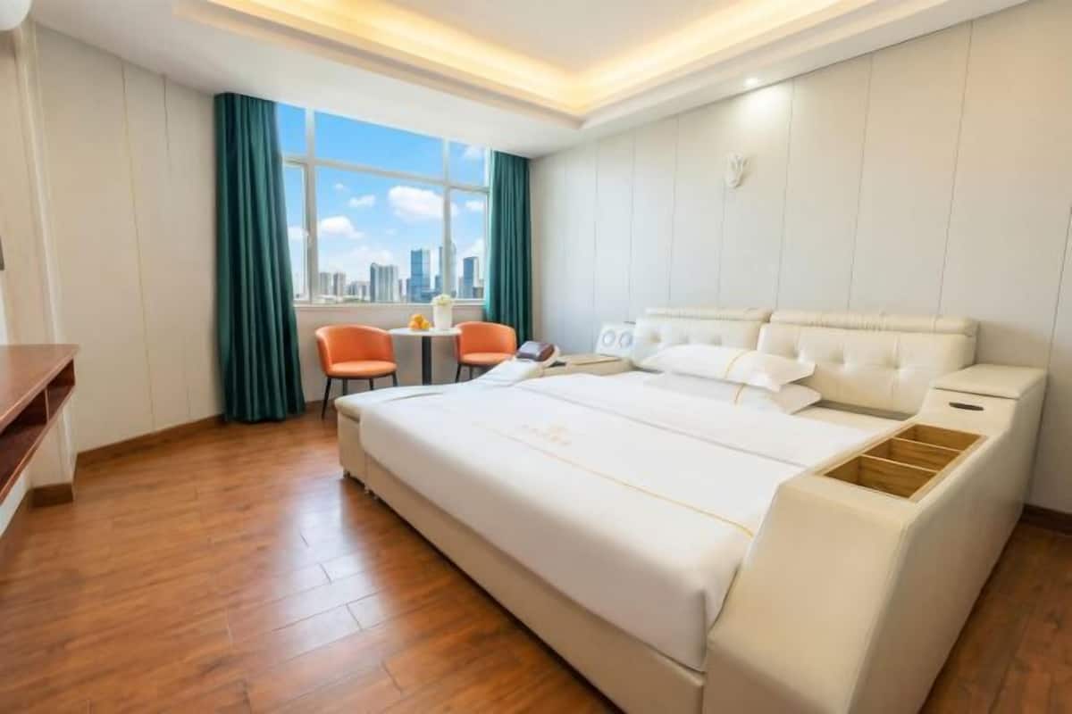 Habitación de hotel con una cama grande, un escritorio y una silla. Se ve la ciudad a través de la ventana.