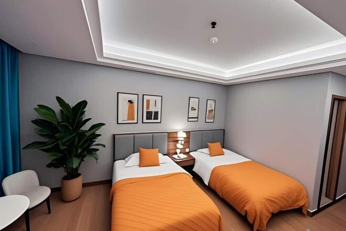Habitación de hotel con dos camas, un escritorio, una silla, una planta en maceta y cuadros en la pared.