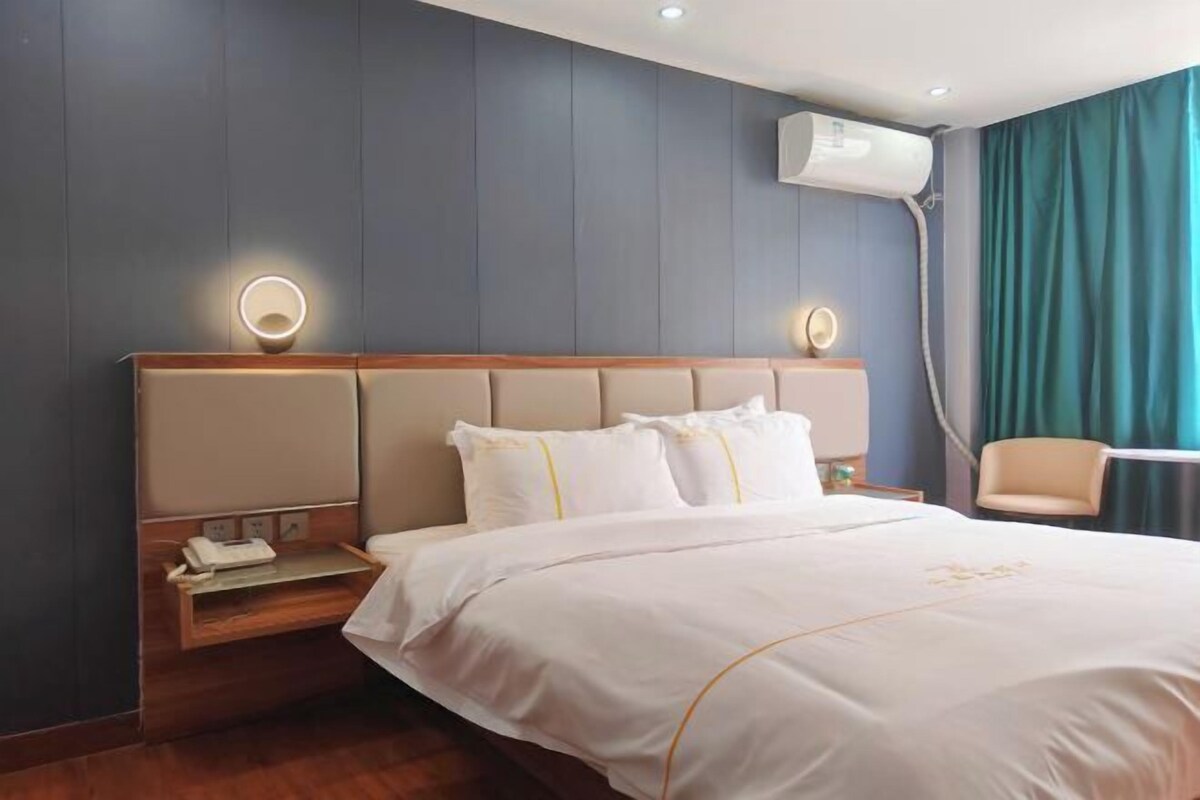 A hotel room with a large bed, bedside tables, a chair, and a window with curtains.