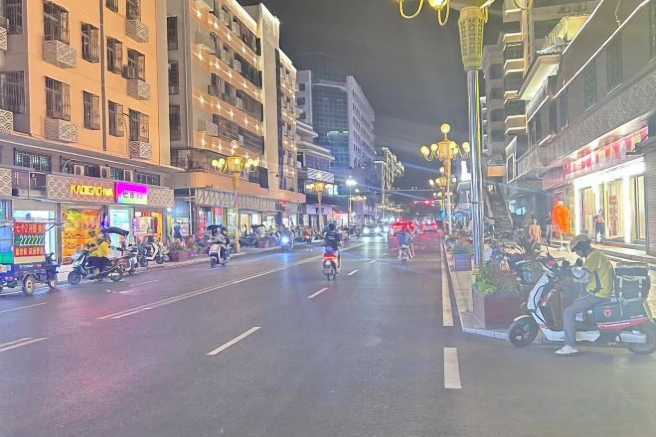 Una strada fiancheggiata da negozi e edifici, con persone e veicoli che la percorrono.