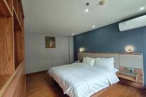 A bedroom with a large bed, a wooden wardrobe, a nightstand, and a wall-mounted air conditioner.