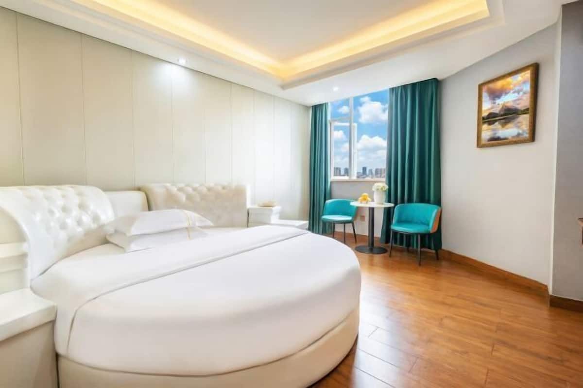 Una habitación de hotel con una cama grande, dos sillas, una mesita, una ventana con cortinas y un cuadro en la pared.