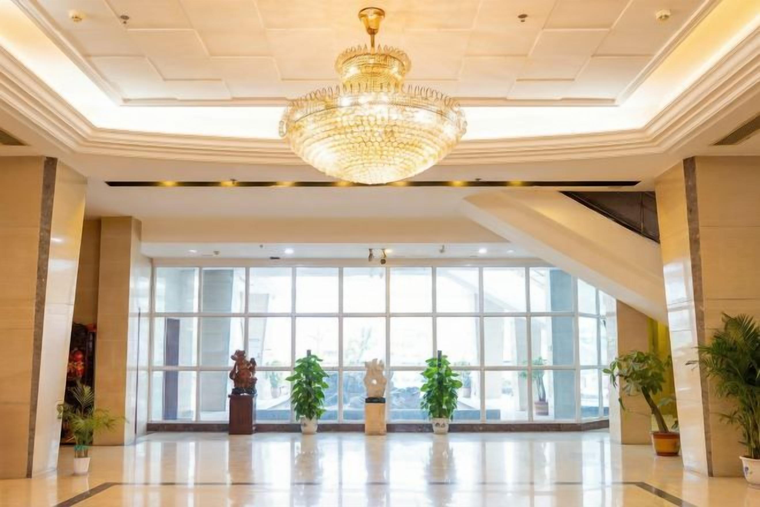 A spacious lobby with a large chandelier, potted plants, and a statue.