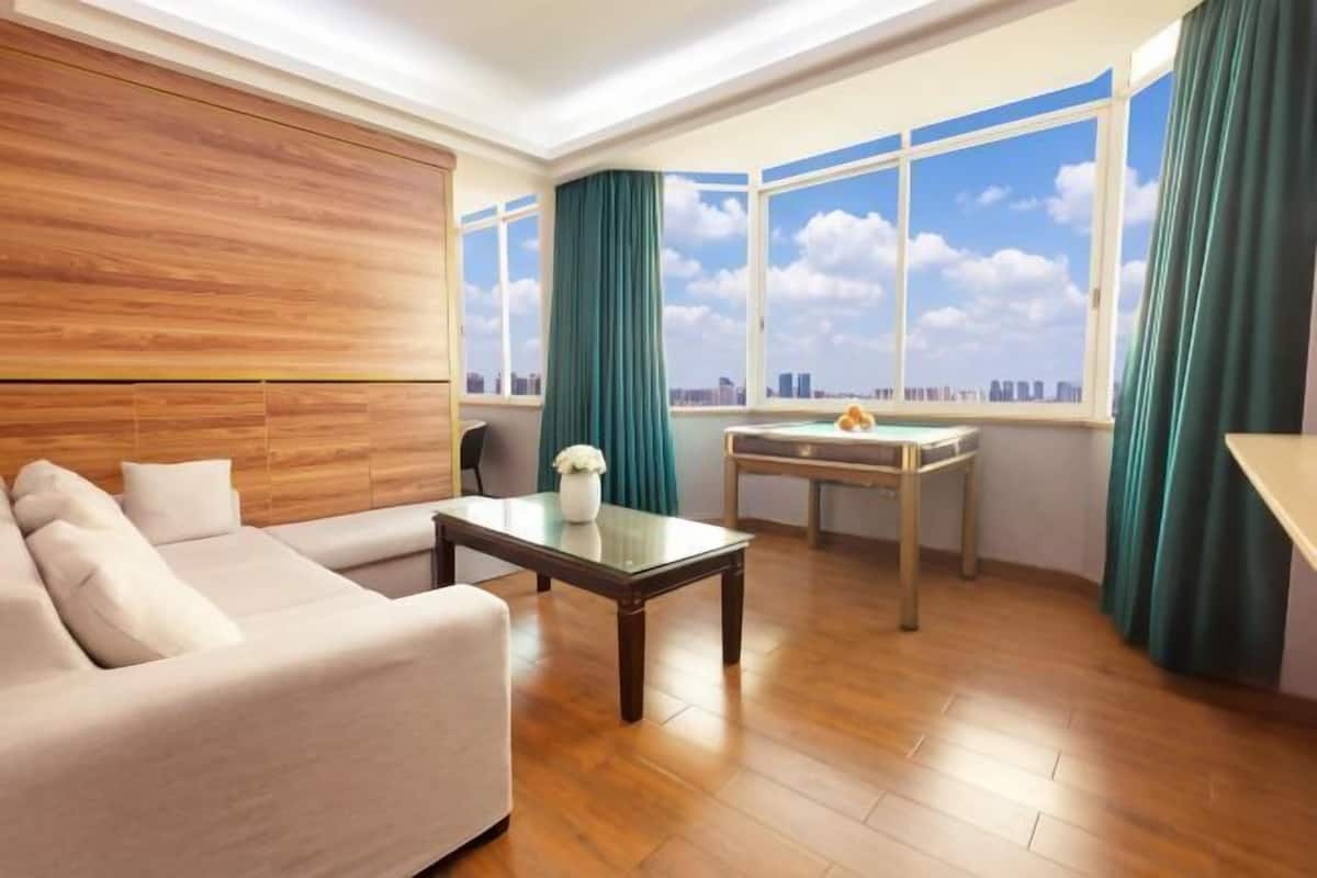 Una sala de estar moderna con un sofá, una mesa de centro y vistas a un paisaje urbano a través de grandes ventanales.