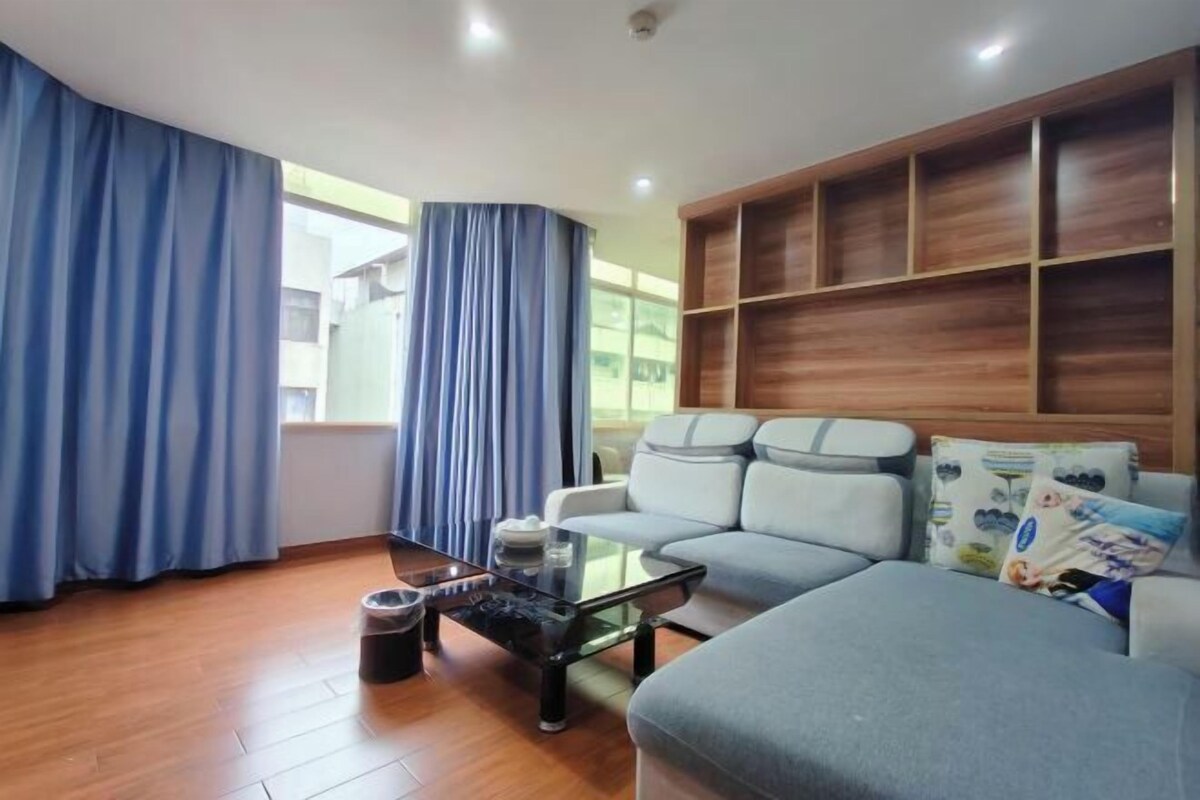 A modern living room with a sofa, a glass coffee table, and a wooden shelving unit.