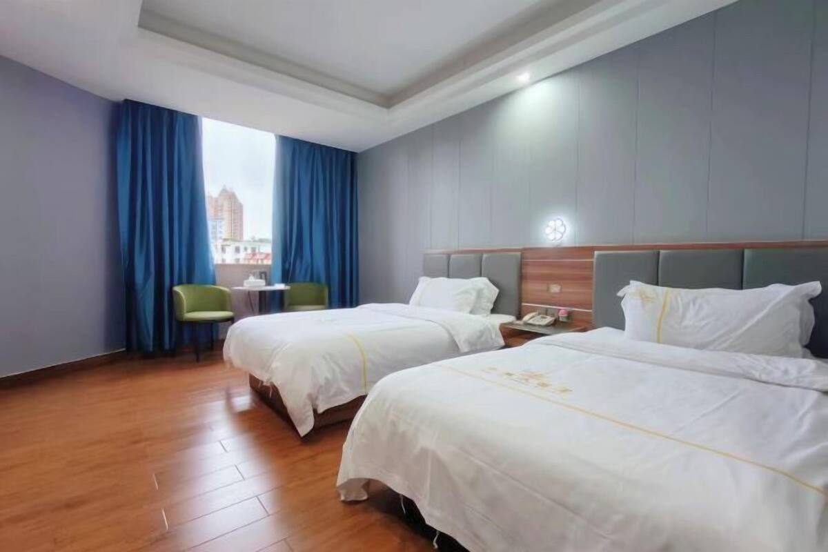 Habitación de hotel con dos camas, un escritorio, una silla y una ventana con cortinas azules.