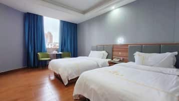 Een hotelkamer met twee bedden, een bureau, een stoel en een raam met blauwe gordijnen.