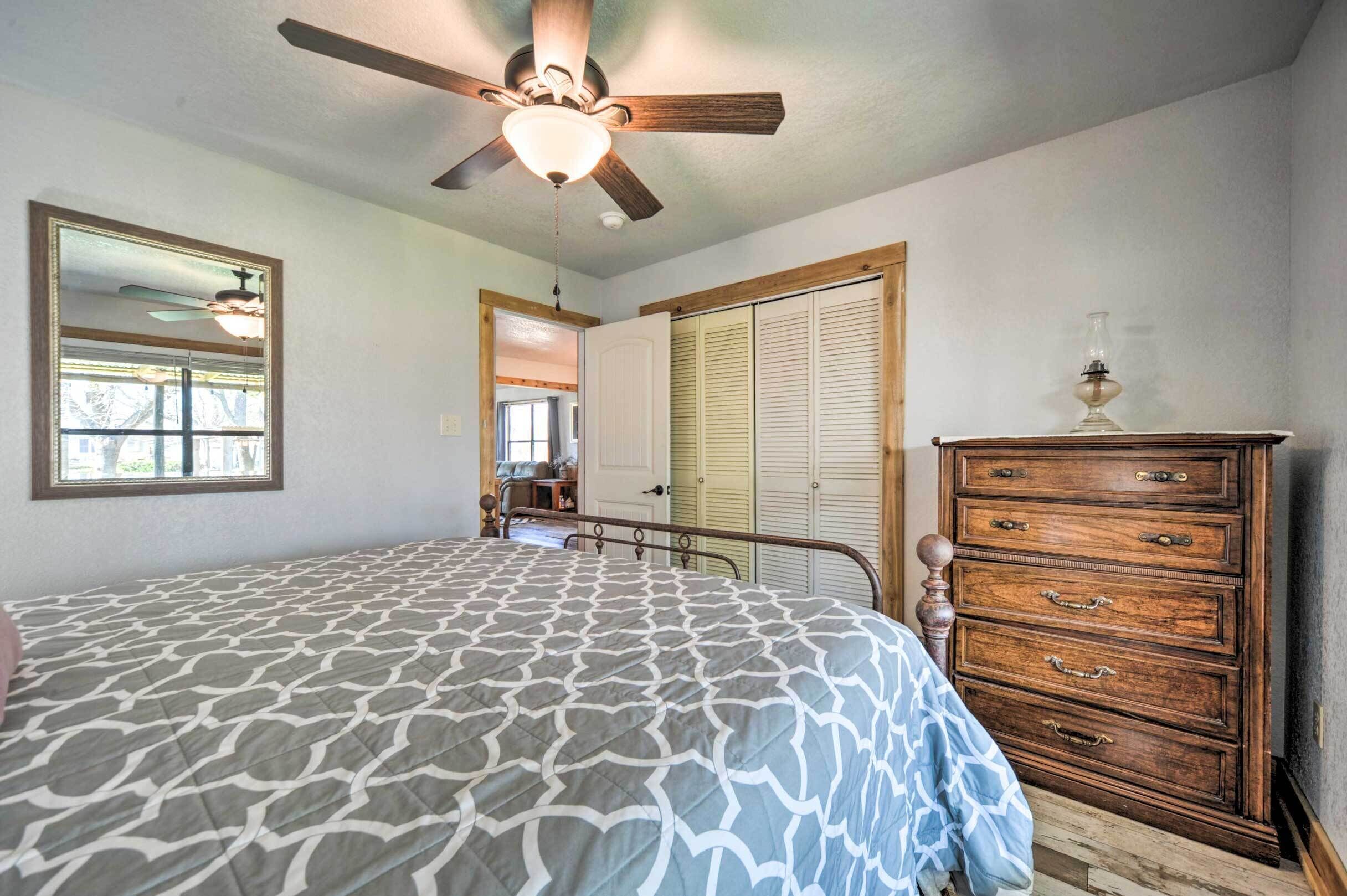 Une chambre à coucher comprenant un lit, une commode, un ventilateur de plafond, un miroir et une porte donnant sur une autre pièce.