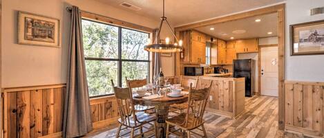 A cozy kitchen with wooden cabinets, a dining table set for four, and a large window providing natural light.