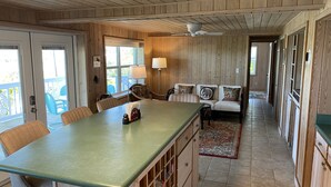Una cocina con una isla de madera, un comedor con sillas, un sofá con cojines estampados y vistas a través de puertas de vidrio.