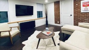 Una sala de estar moderna con un televisor de pantalla plana, una chimenea, un sofá blanco, una mesa de centro y un tapete de cuero de vaca.