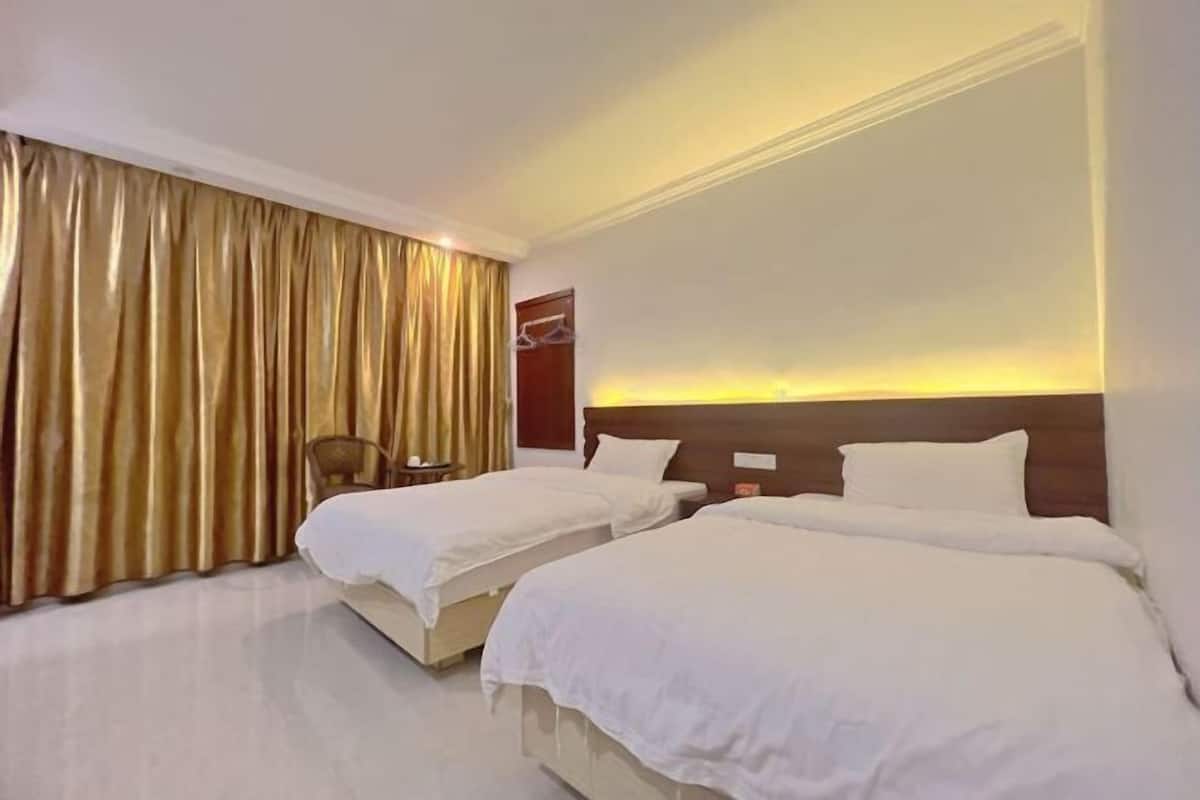 Habitación de hotel con dos camas, un ventanal con cortinas, una mesita y una silla.
