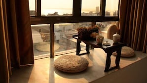 A room with a large window, a wooden table with a vase of flowers, and woven poufs on the floor. - Red Bay Hesheng Homestay (Shanwei)