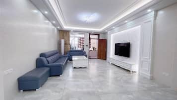 A modern living room with a sectional sofa, a flat-screen TV, and a marble floor.