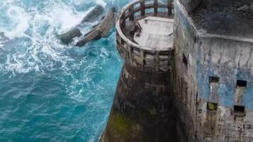 Una estructura cilíndrica de concreto con una abertura circular en la parte superior, cerca de una masa de agua.