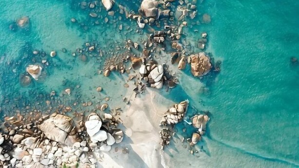 An aerial view of a beach with scattered rocks and clear turquoise water. - Red Bay Hesheng Homestay (Shanwei)
