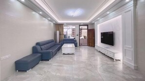 A modern living room with a sectional sofa, a coffee table, a TV on a stand, and a decorative ceiling light. - Red Bay Hesheng Homestay (Shanwei)