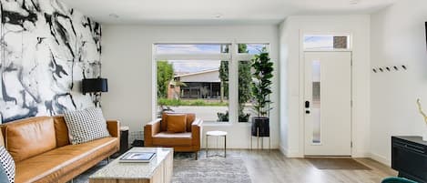 A modern living room with a leather sofa, a coffee table, a side table, and a large abstract painting on the wall.