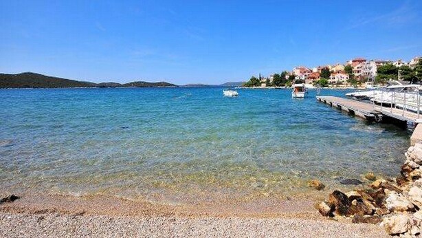 A coastal scene with clear water, a rocky shoreline, and buildings in the background. - Apartments & Rooms Villa Petra - One Bedroom Apartment with Balcony and Sea View - 2 (Žaborić)