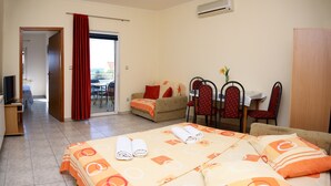A hotel room with a bed, a sofa, a dining area with chairs, and a TV. - Apartments & Rooms Villa Petra - One Bedroom Apartment with Balcony and Sea View - 2 (Žaborić)