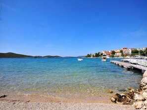 A coastal scene with clear water, a rocky shoreline, and buildings in the background. - Apartments & Rooms Villa Petra - One Bedroom Apartment with Balcony and Sea View - 3 (Žaboric)