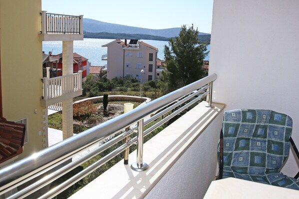 A balcony with a metal railing, a chair, and a view of a body of water and buildings in the background. - Apartments & Rooms Villa Petra - One Bedroom Apartment with Balcony and Sea View - 3 (Žaboric)
