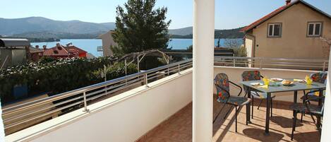 A balcony with a table and chairs, overlooking a lake and mountains.