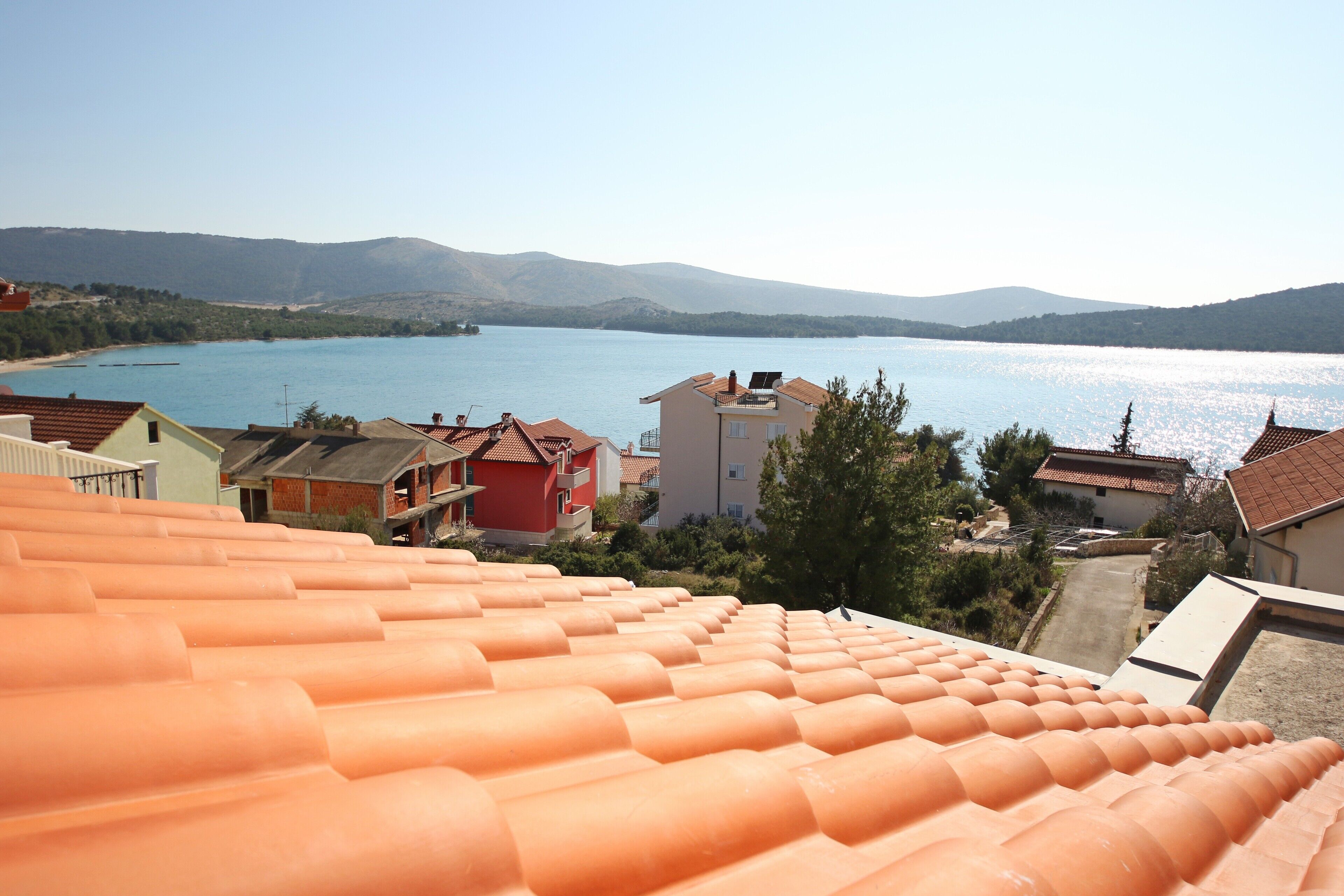 A coastal view with terracotta roofs, a body of water, and distant mountains.