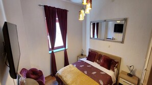 A bedroom with a bed, a desk, a chair, a mirror, and a window with curtains. - Rooms Argo - Red Double Room (Cres)