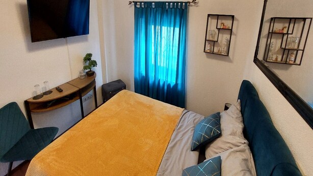 Una habitación de hotel con cama, escritorio, televisión y ventana con cortinas.