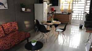 Ein modernes Wohnzimmer mit Sofa, Stühlen, einem Esstisch und einer Küchenzeile mit Schränken und einem Kühlschrank.