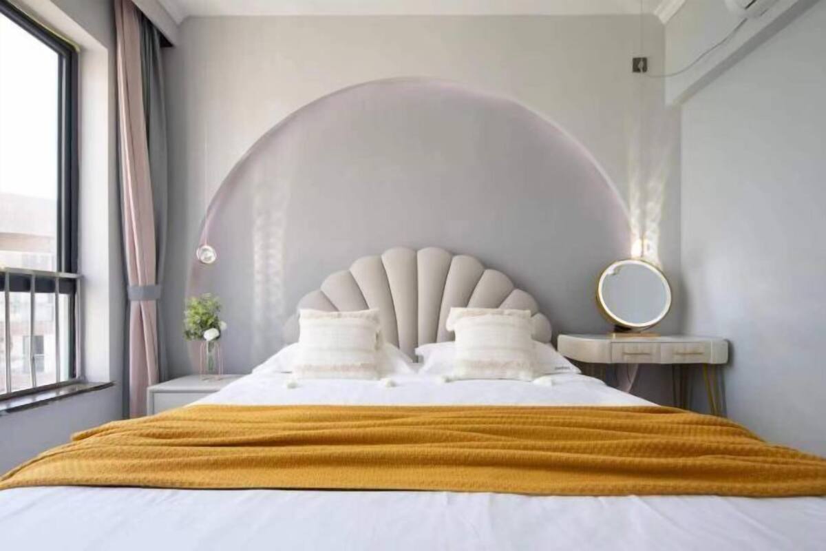 Une chambre moderne avec un grand lit, un miroir rond et une arche décorative sur le mur.
