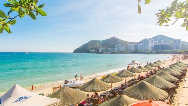 A beach with thatched umbrellas and a clear view of the ocean and a cityscape in the background. - Jiuqi · Youran Seaside Holiday Apartment (Sanya)