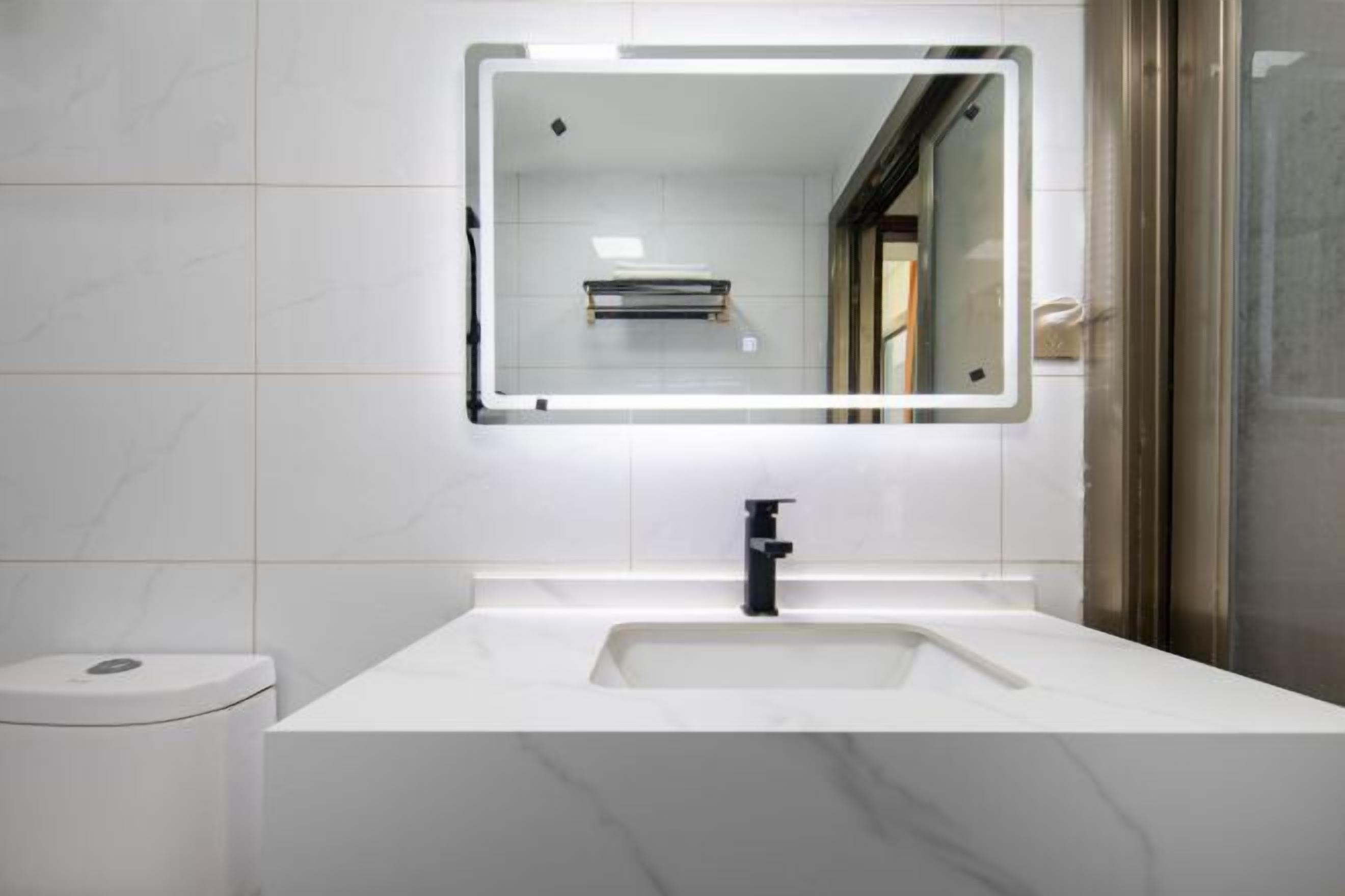 A modern bathroom with a white sink, a black faucet, and a mirror with built-in lighting.