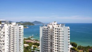 A high-rise hotel with multiple floors, overlooking a coastal area with clear blue waters and distant islands. - Jiuqi · Youran Seaside Holiday Apartment (Sanya)
