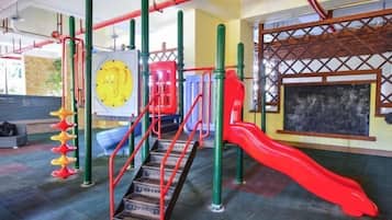 Un parque infantil con un tobogán rojo, estructuras para escalar y una zona de juegos circular amarilla.