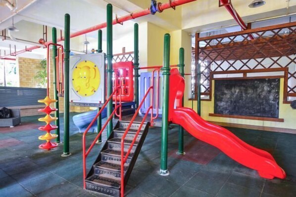 Ein Spielplatz mit einer roten Rutsche, Klettergerüsten und einem gelben, kreisförmigen Spielbereich.