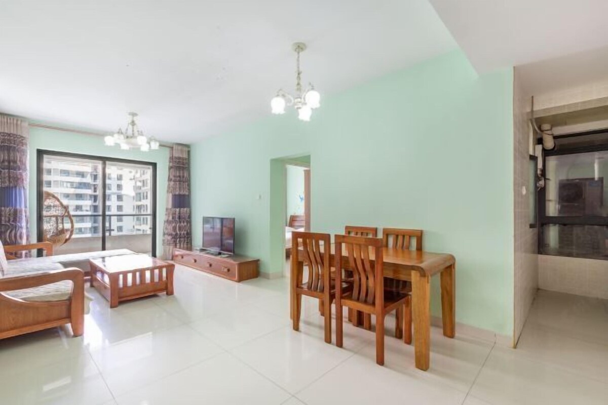 Ein geräumiges Wohnzimmer mit Essbereich, Fernseher und Blick auf ein Gebäude durch große Fenster.