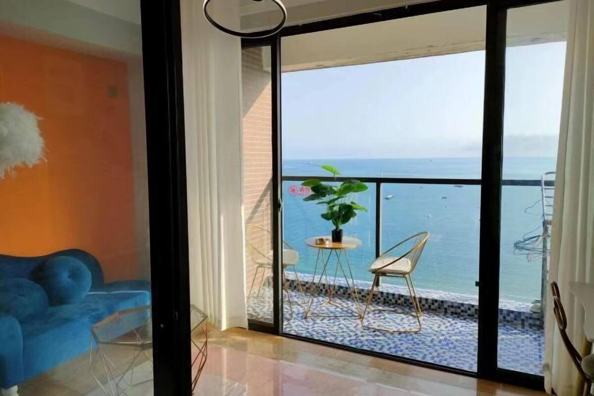 Un balcon avec vue sur la mer, un canapé bleu et une petite table avec une plante.