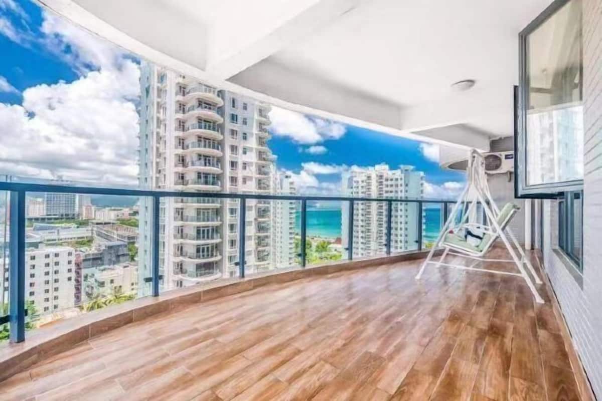 Un balcon spacieux doté d’un plancher en bois, d’une chaise blanche et offrant une vue sur des immeubles de grande hauteur et une plage.